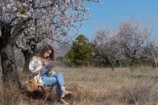 Donna seduta su una sedia sotto un campo di alberi in fiore mentre disegna