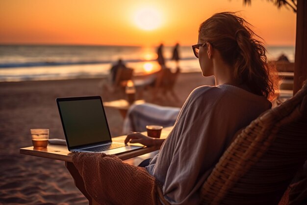 donna seduta su una spiaggia con un computer portatile e un tramonto sullo sfondo