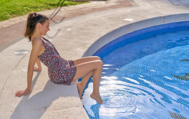 Donna seduta sul bordo della piscina a prendere il sole in un vestito con i piedi nell'acqua