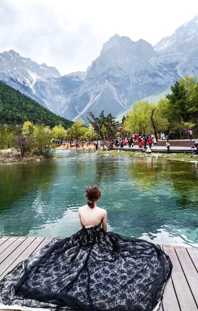Donna seduta sul molo sul lago contro le montagne