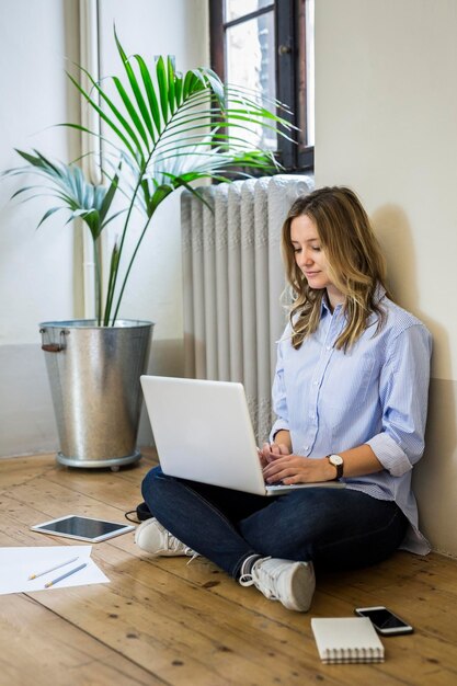 Donna seduta sul pavimento a casa utilizzando il computer portatile