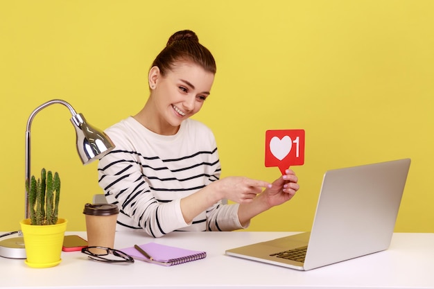 Donna seduta sul posto di lavoro che chiede di valutare i suoi post che mostrano il modello del contatore dei Mi piace sullo schermo del laptop