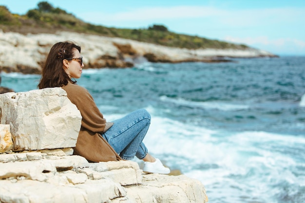 Donna seduta sulla scogliera godendo della vista del mare giornata di sole ventoso