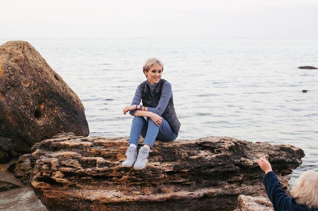 Donna seduta sulla scogliera vicino al mare in autunno o in estate