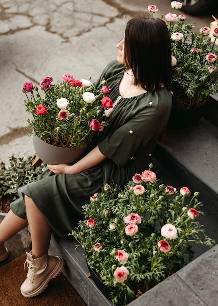 Donna seduta sulle scale in un negozio di fiori che tiene un grande vaso di fiori con fiori di ranuncolo