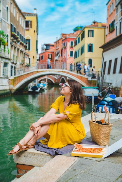 Donna seduta sullo stagno con vista sul canale di venezia che mangia pizza