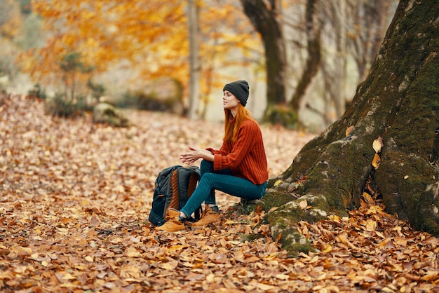 Donna seduta vicino a un albero nella foresta autunnale e foglie cadenti parco paesaggio foto di alta qualità