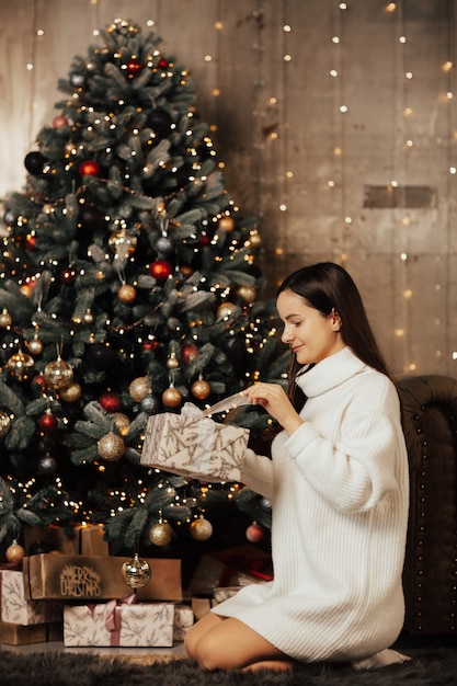 Donna seduta vicino all'albero di Natale e apertura confezione regalo.