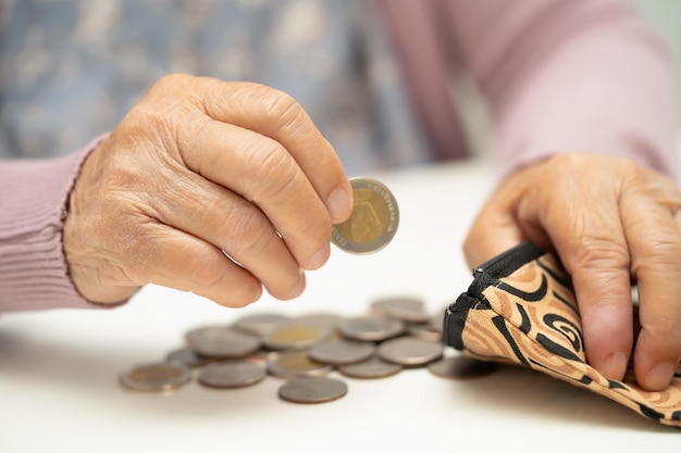 Donna senior asiatica che tiene il conteggio dei soldi della moneta in borsa Problema di risparmio di povertà in pensione