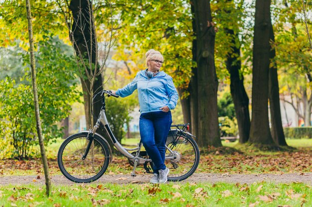 donna senior che cammina nel parco con una bicicletta