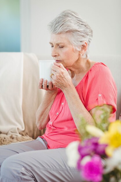 Donna senior che odora una tazza di caffè a casa