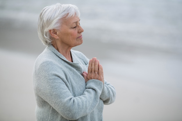 Donna senior che prega sulla spiaggia