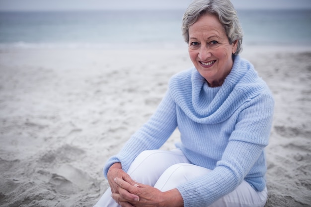 Donna senior felice che si siede sulla spiaggia