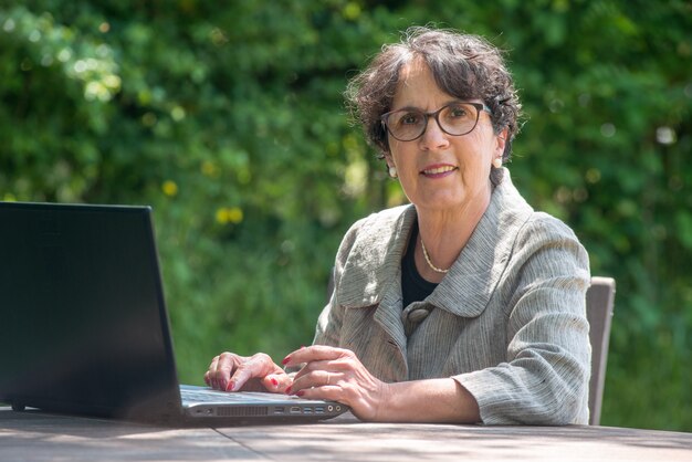 Donna senior felice che utilizza computer portatile nel giardino