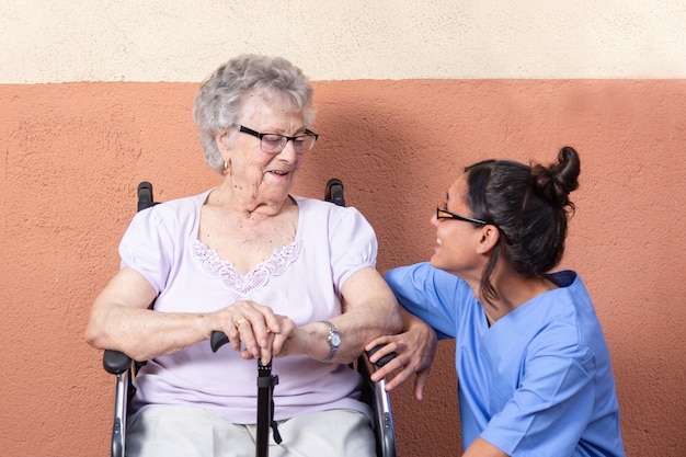 Donna senior felice con il bastone da passeggio in sedia a rotelle con il suo badante a casa