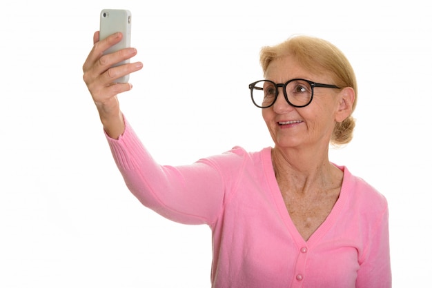 Donna senior felice del nerd che sorride e che prende selfie con il telefono cellulare