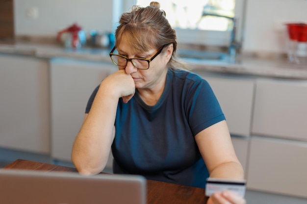 Donna senior pensionata frustrata che si siede sul sofà a casa facendo uso del computer portatile