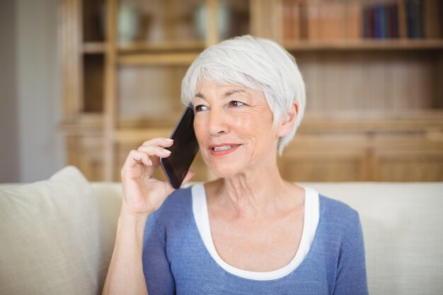 Donna senior sorridente che parla sul telefono cellulare in salone