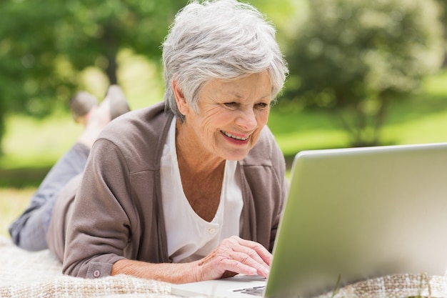 Donna senior sorridente che per mezzo del computer portatile al parco