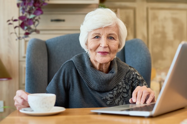 Donna senior sorridente che per mezzo del computer portatile