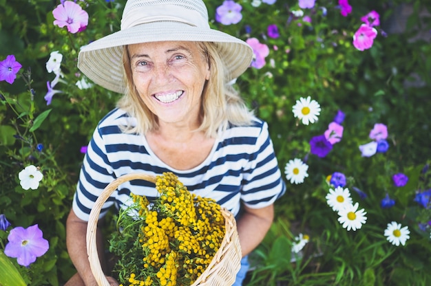 Donna senior sorridente felice che posa nel giardino estivo con fiori