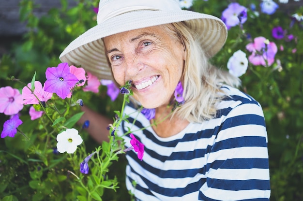 Donna senior sorridente felice che posa nel giardino estivo con fiori