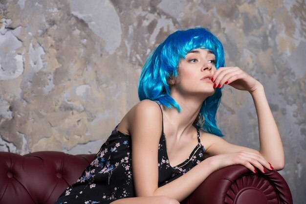 Donna sensuale con parrucca di capelli blu. La donna con i capelli alla moda si rilassa sul sofà. Ragazza di bellezza con look e trucco glamour. Modello di moda con manicure per unghie rossa. Acconciatura di bellezza e moda.