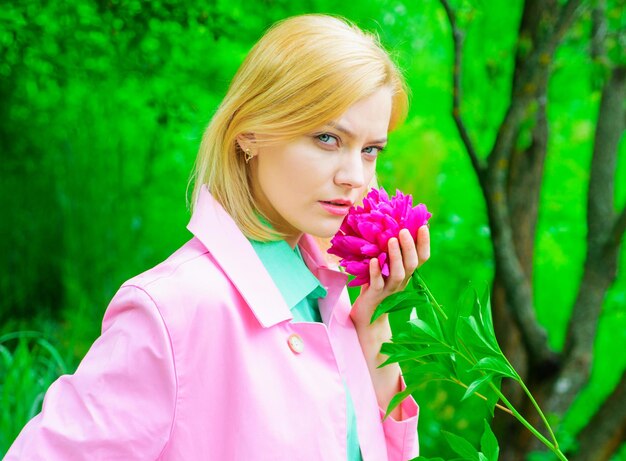 Donna sensuale in cappotto rosa con fiore di peonia nel parco Ragazza romantica con peonie in giardino primaverile