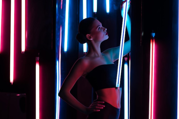 Donna sensuale per tutto il corpo con lampada luminosa appoggiata al muro in una stanza buia con illuminazione al neon