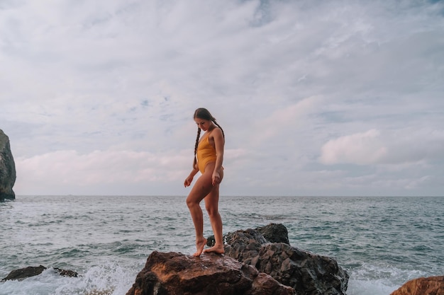 Donna sensuale spensierata felice del fuoco selettivo con i capelli lunghi in costume da bagno nero che posa alla spiaggia del tramonto