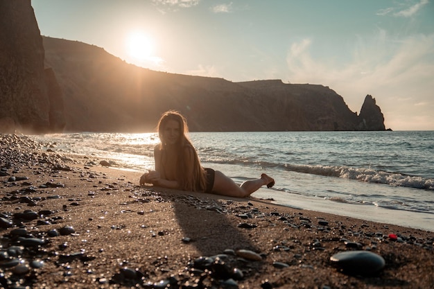 Donna sensuale spensierata felice del fuoco selettivo con i capelli lunghi in costume da bagno nero che posa alla spiaggia del tramonto