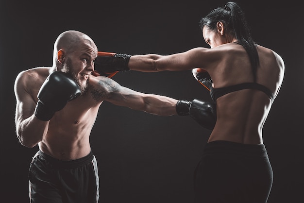 Donna senza camicia che si esercita con l'allenatore alla lezione di boxe e autodifesa, studio, spazio buio