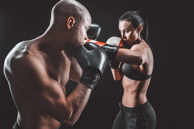 Donna senza camicia che si esercita con l'allenatore alla lezione di boxe e autodifesa, studio, spazio buio