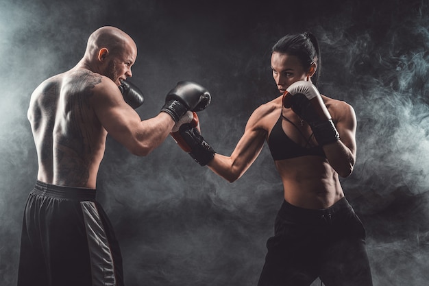 Donna senza camicia che si esercita con l'allenatore alla lezione di boxe e autodifesa, studio, spazio buio