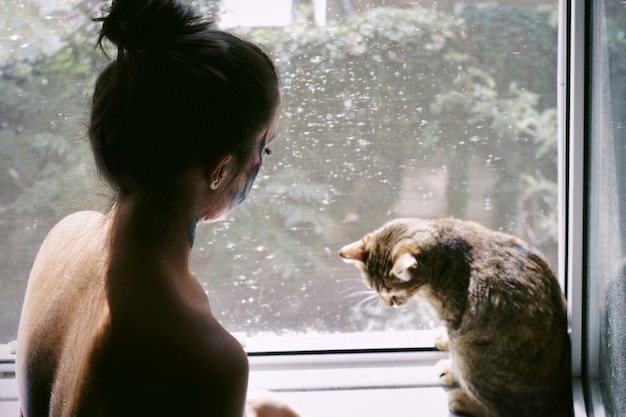 Donna senza camicia con il gatto sul davanzale della finestra