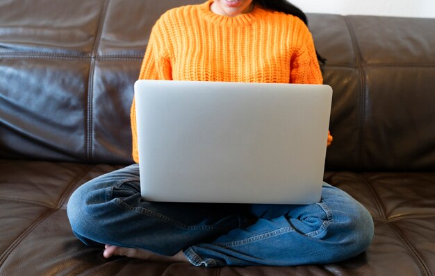 Donna senza volto che utilizza il computer sul divano di casa