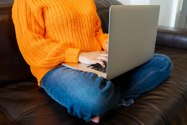 Donna senza volto che utilizza il computer sul divano di casa