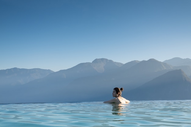 Donna sexy che si rilassa nella piscina di infinito che esamina Mountain View sbalorditivo il concetto lussuoso vacanza / della località di soggiorno