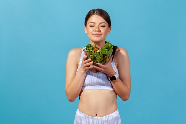 Donna snella che chiude gli occhi godendosi l'aroma di insalata di verdure fresche, alimentazione sana, dieta disintossicante