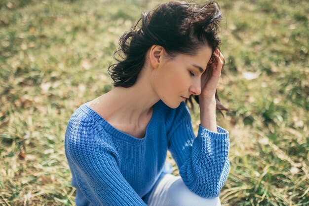 Donna sognante con gli occhi chiusi con la mano sul viso Ritratto di giovane donna caucasica bruna attraente con capelli ventosi che sogna fuori in primavera o in estate seduto nel parco Concetto di stile di vita