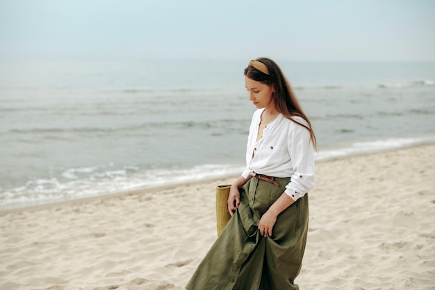 Donna sognante con i capelli scuri che cammina da sola sulla spiaggia vicino al mare