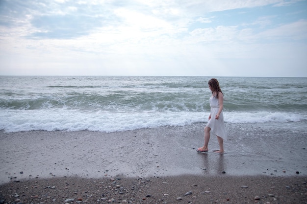 Donna sola in abito bianco che cammina lungo la spiaggia