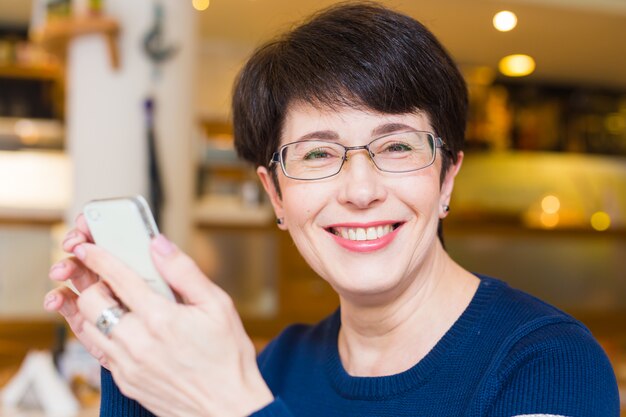 Donna sorridente attraente che per mezzo del telefono cellulare