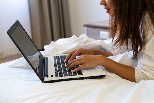 Donna sorridente attraente che si rilassa sul letto facendo uso del computer della compressa.