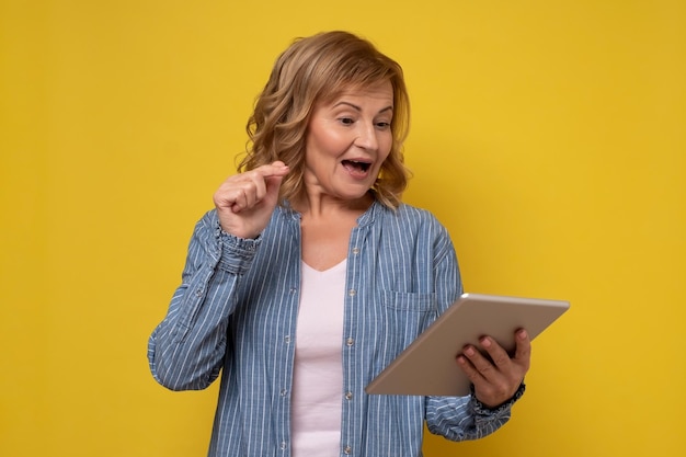 Donna sorridente attraente matura che utilizza un computer tablet selezionando le merci nel negozio online