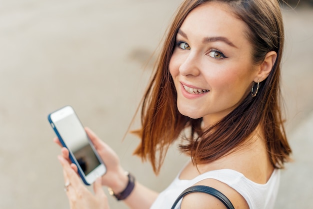 Donna sorridente bella con il telefono cellulare che cammina sulla strada