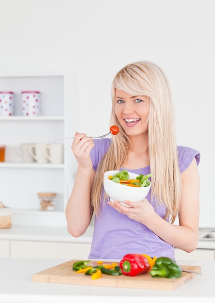 Donna sorridente bionda che mangia la sua insalata