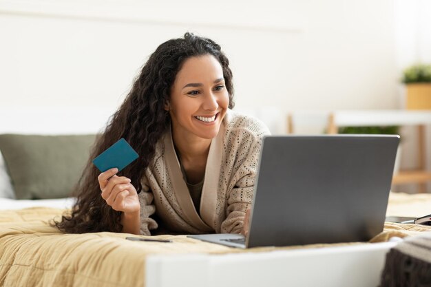 Donna sorridente casuale che utilizza pc e carta di credito a casa