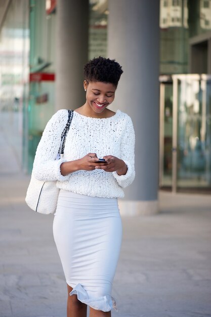Donna sorridente che cammina sul marciapiede e invio di messaggi di testo