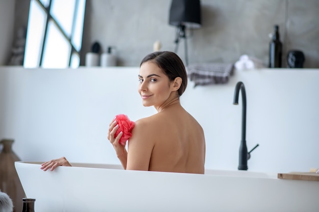 Donna sorridente che cattura un bagno rilassante con una spugna